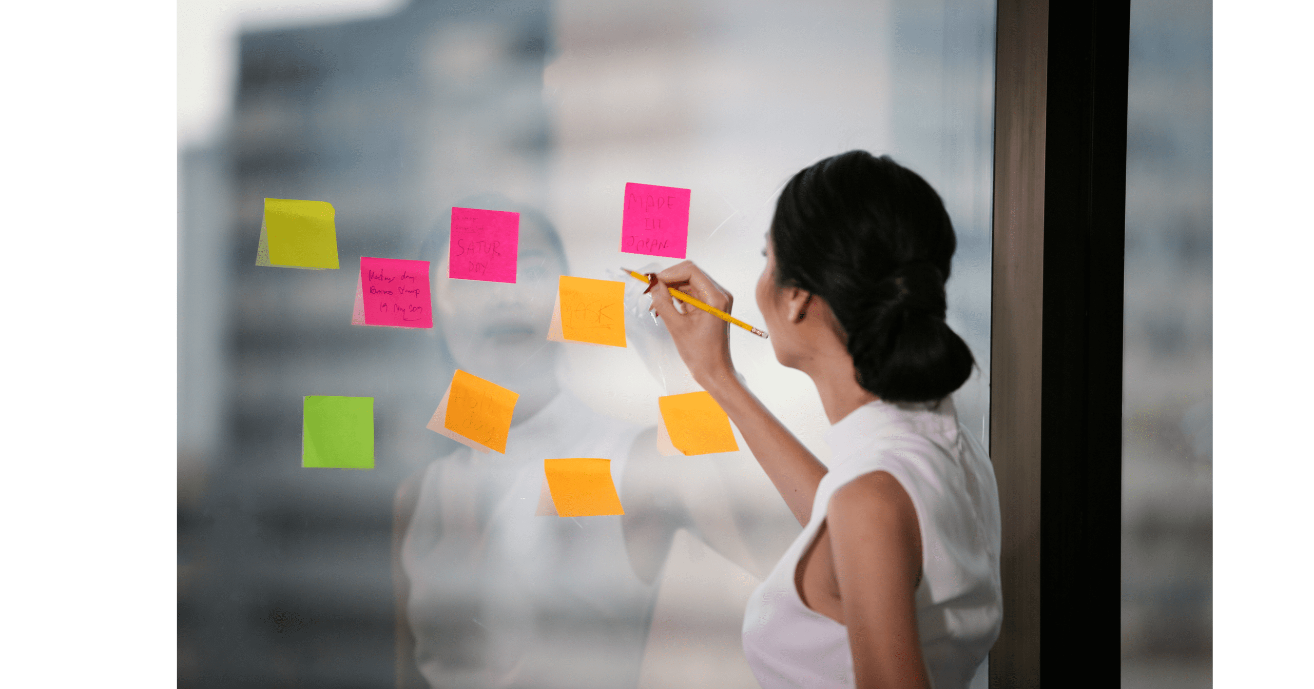 Woman writing on colorful sticky notes on a glass window in an office.